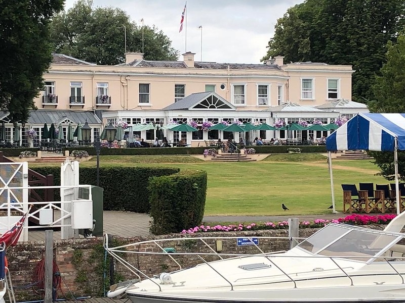 Phyllis Court at Henley seen from the river, with parasols on the lawn and boats moored at the bank